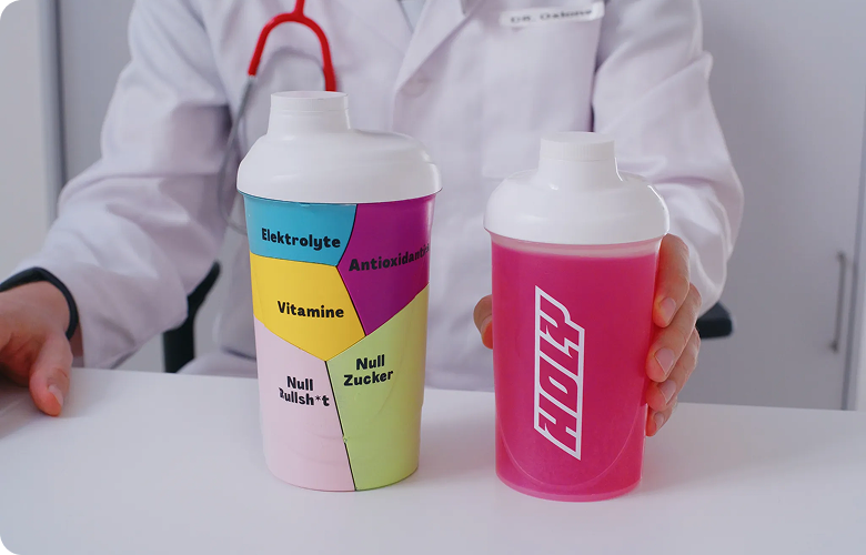 Zwei bunte Shaker stehen auf einem Tisch; eine Person in weißem Kittel hält einen Shaker in der Hand.