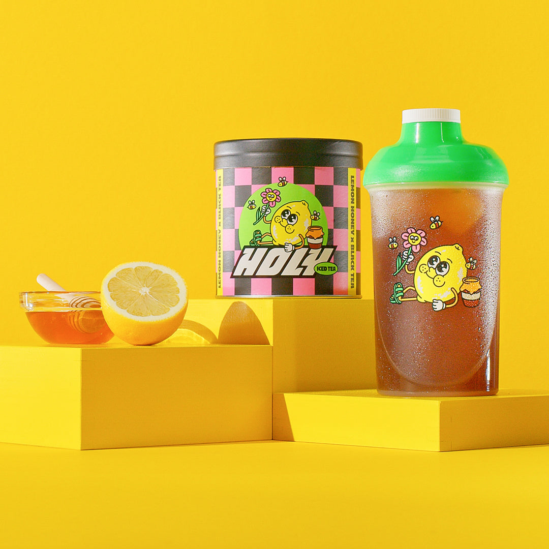 Pappdose und Shaker mit Zitronenmotiv, eine halbe Zitrone und Honigschale vor gelbem Hintergrund.