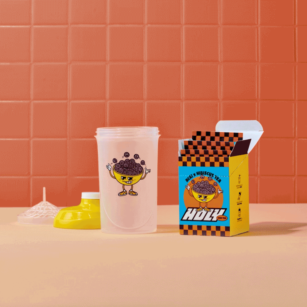 Shaker und geöffnete Pappbox mit Probepackungen vor einer roten Kachelwand.