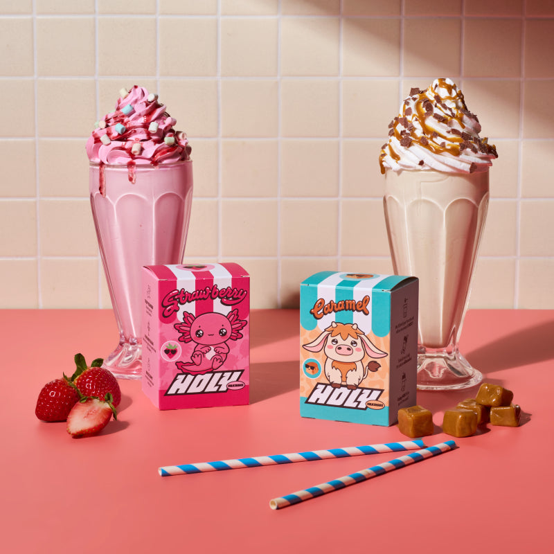 Zwei Shakes mit Sahne und Streuseln hinter Pappboxen mit Erdbeer- und Karamellgeschmack, daneben Früchte und Süßigkeiten.
