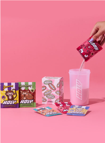 Person füllt einen Shaker mit Pulver aus einem Sachet, umgeben von verschiedenen Probepackungen und einer Pappdose.