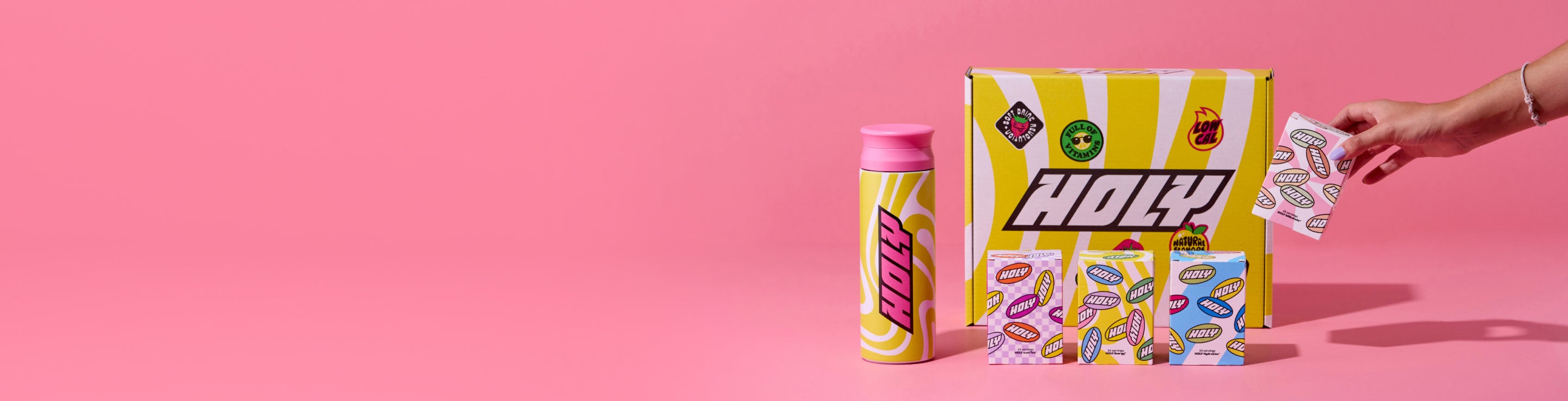 Gelber Shaker, Pappboxen mit Probepackungen auf rosa Hintergrund, eine Hand nimmt eine Packung.