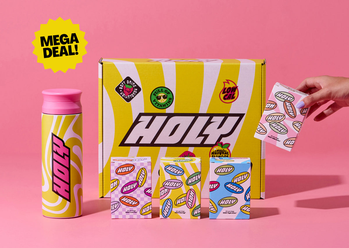 Eine gelbe Box mit "Holy"-Logo, daneben ein Shaker und drei Pappdosen mit mehreren Probepackungen auf rosa Hintergrund.