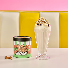 Pappdose mit Haselnussmuster und eine Milchshake in einem durchsichtigen Glas, dekoriert mit Sahne und Schokostückchen.