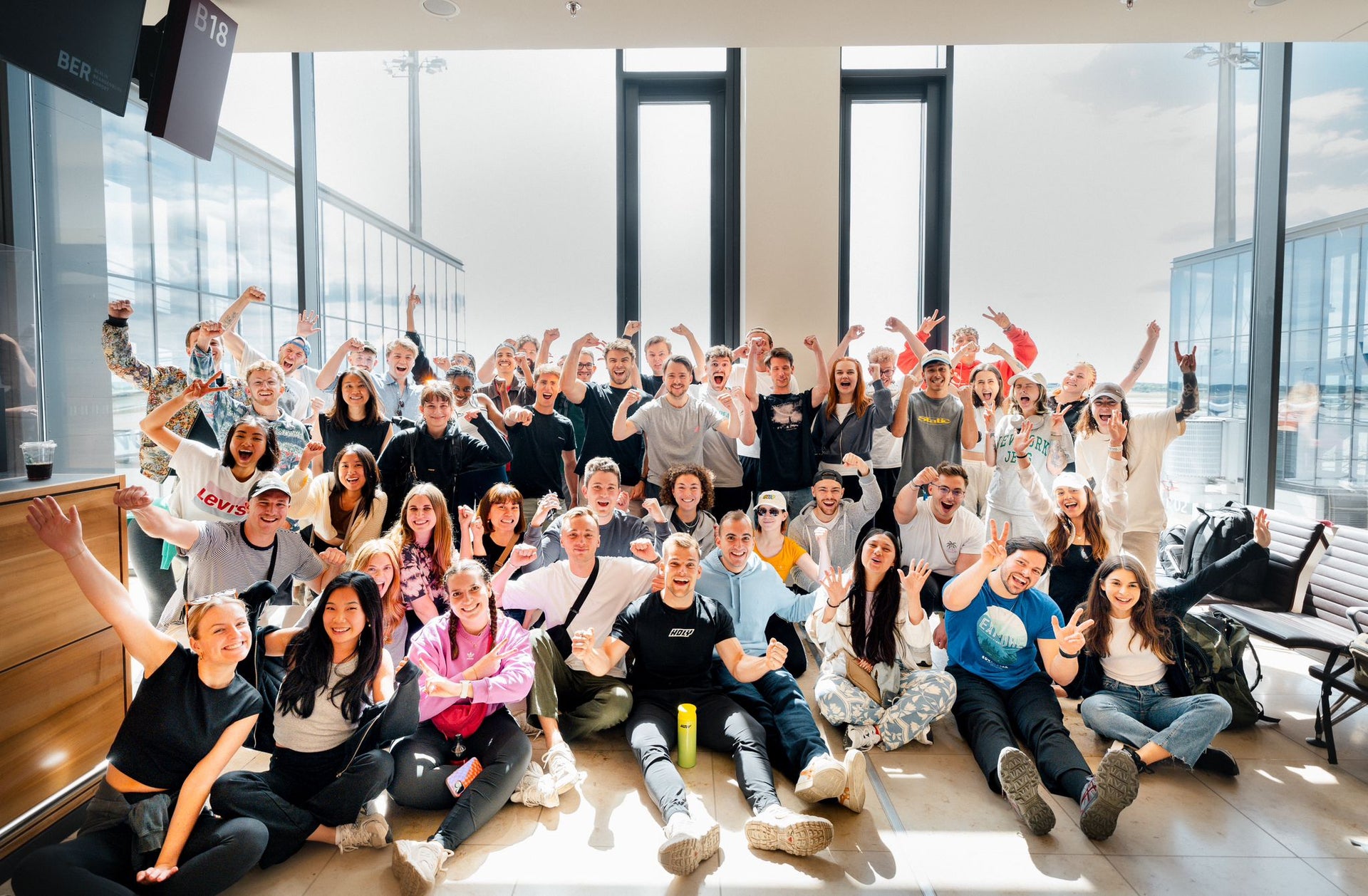 Gruppe von Menschen, die in einem lichtdurchfluteten Raum fröhlich posieren und die Hände in die Luft strecken.