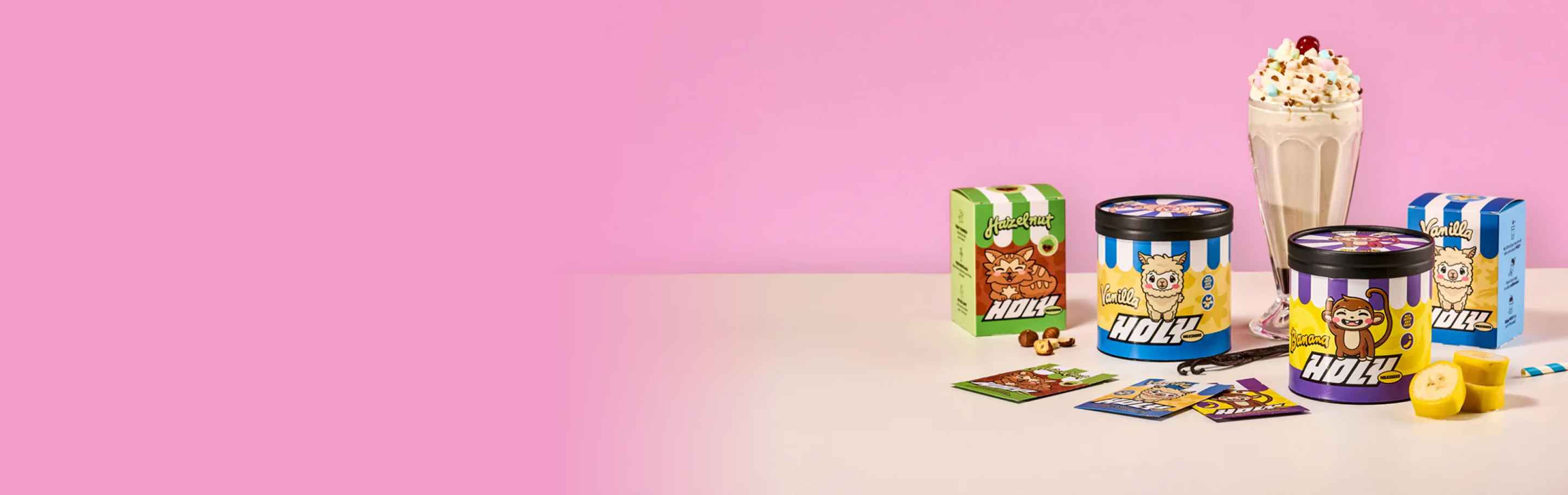 Pappdosen, Pappboxen mit Probepackungen, ein Milchshake und Bananenstücke auf einem Tisch vor einem rosa Hintergrund.